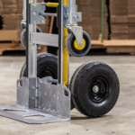 Heavy-duty hand truck with black wheels and silver frame, in warehouse setting.