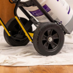 Black utility cart with yellow handles and a white bucket on a light cloth. Gorilla Made wheel.