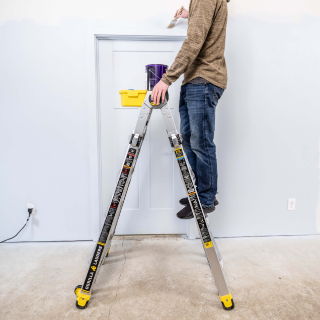 Person standing on a Gorilla Made ladder painting a wall. Ladder features yellow accents.