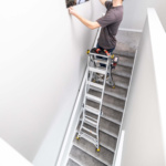 Person on a multi-position Gorilla Made ladder on stairs, hanging a picture.