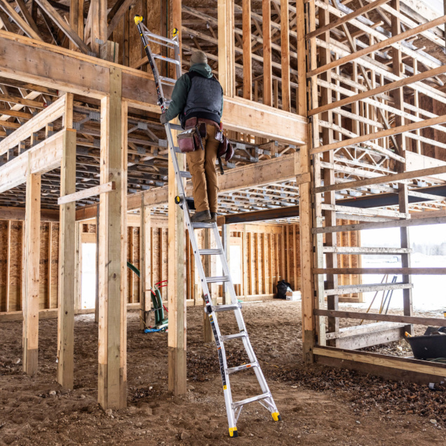 Person climbing a silver Gorilla Made ladder in a wooden construction site.