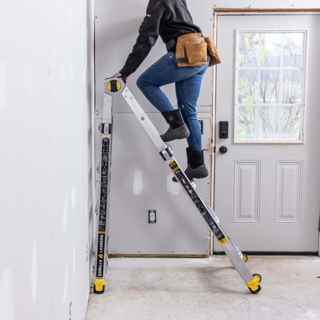 Person using Gorilla Ladders' adjustable ladder indoors, near a white door.