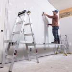 Silver Gorilla Ladders forming a scaffold, person working on a white drywall.