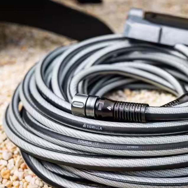 Coiled black and gray Gorilla ToughLite garden hose on a gravel surface.