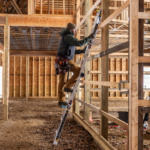 Person climbing a silver Gorilla Made ladder in a wooden construction site.