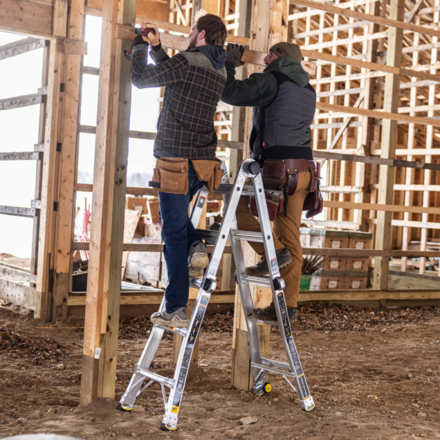 Two people working on wooden beams using a sturdy Gorilla Made ladder indoors.