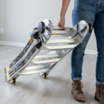 Person holding folded Gorilla Made aluminum ladder with black and orange accents.