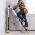 Person climbing Gorilla Made ladder indoors with tool belt, yellow warnings visible.