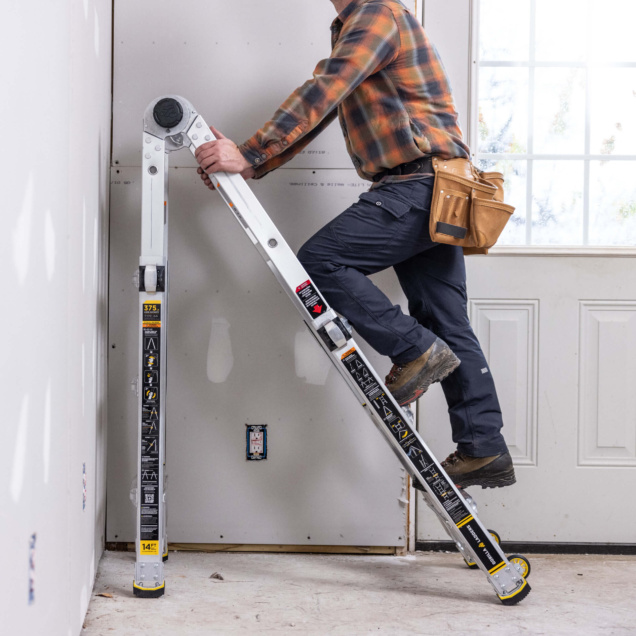 Person climbing Gorilla Made ladder indoors with tool belt, yellow warnings visible.