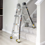 Adjustable silver ladder on stairs with text "GMPX 14W COM Image 9 01" on label.