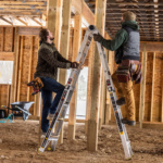 Two people using a silver Gorilla Made ladder in a construction site.