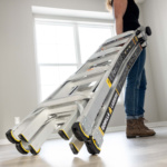 Person carrying a silver Gorilla Ladders ladder indoors.