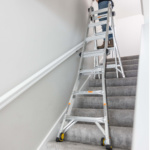 Silver adjustable ladder set up on carpeted stairs for indoor use.