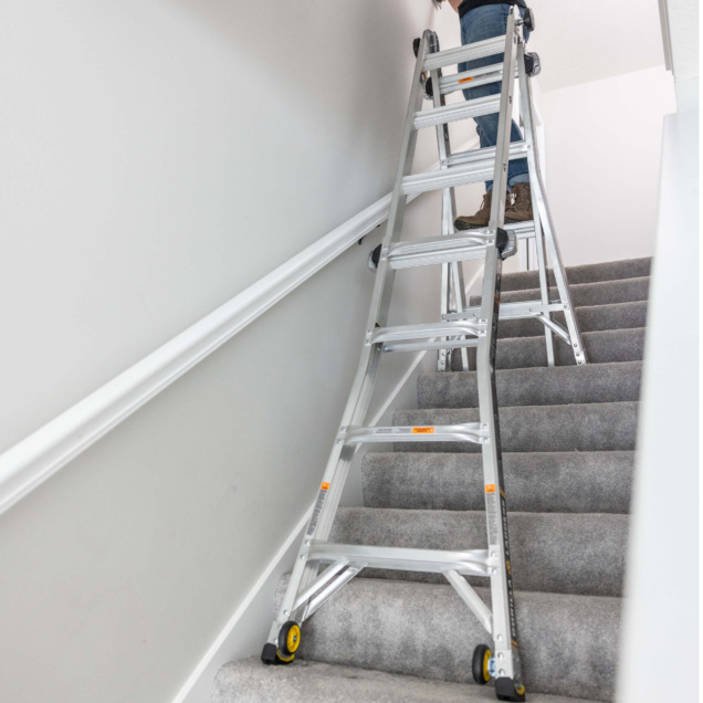 Silver adjustable ladder set up on carpeted stairs for indoor use.