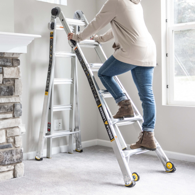 Person on silver Gorilla Ladders ladder near stone fireplace in a carpeted room.