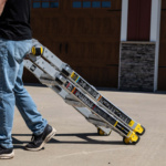 Man pulling silver Gorilla Made ladder with yellow wheels on a driveway.