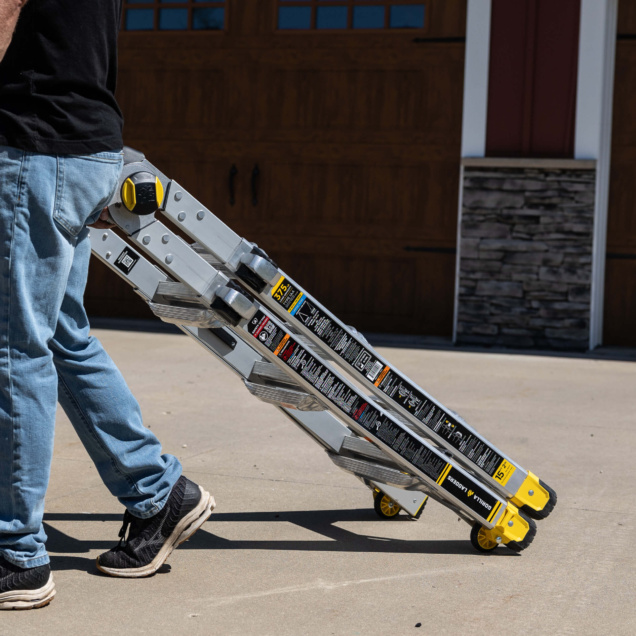Man pulling silver Gorilla Made ladder with yellow wheels on a driveway.