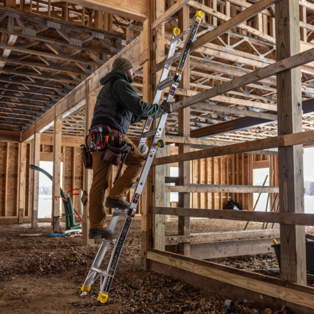 Person using a Gorilla Made ladder with yellow accents in a wooden construction site.