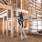 Person climbing a Gorilla Made ladder in a wooden building under construction.