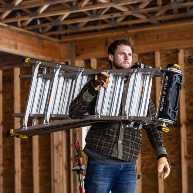 Person holding a silver Gorilla Ladders ladder in a construction setting.