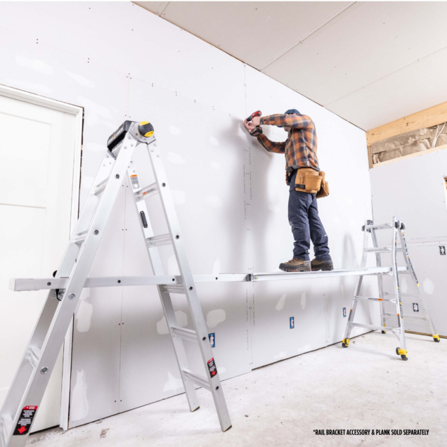 Worker using ladder and plank setup to install drywall. Text: "RAIL BRACKET ACCESSORY & PLANK SOLD SEPARATELY".