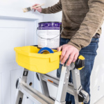Person using Gorilla Made ladder with yellow tray holding paint can and tape.