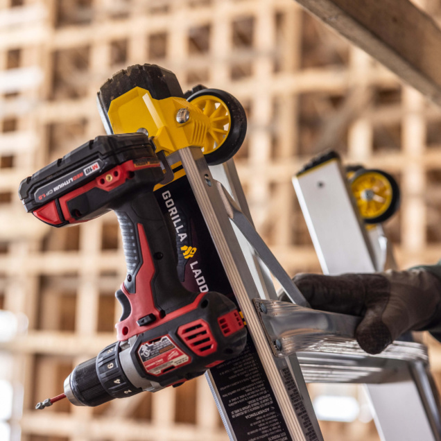 Close-up of Gorilla Ladder with attached red and black drill, yellow wheels visible.