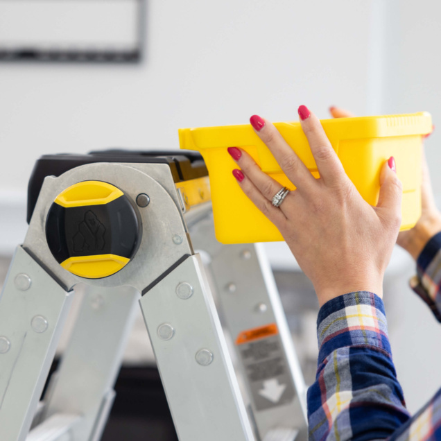 Close-up of a Gorilla Made ladder with a person placing a yellow bin on top.
