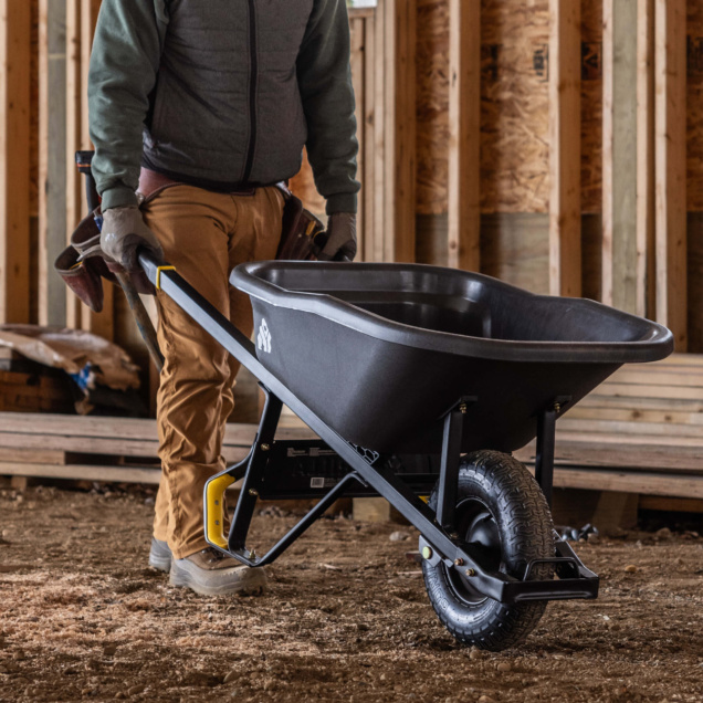 Person using a black Gorilla Made wheelbarrow indoors on a construction site.