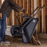 Person using Gorilla Made black wheelbarrow with yellow grips inside a construction site.