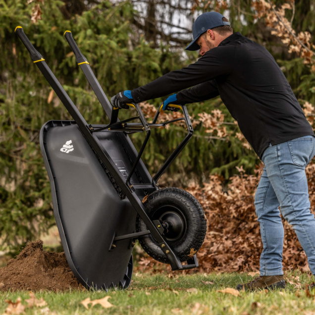 Man using black Gorilla Made wheelbarrow on grass. GPXD 6C logo visible.