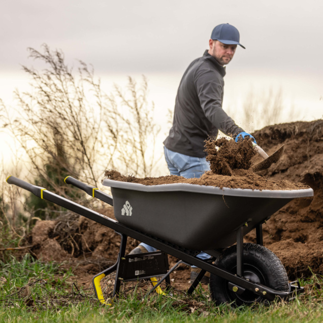 Gorilla Made heavy-duty black wheelbarrow filled with soil, used on rugged terrain.