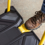 Brown boot stepping on a yellow foot pedal of a black Gorilla Made utility cart.
