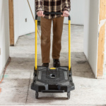 Person pushing a black Gorilla utility cart with yellow handles in a hallway.