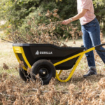 Person using black Gorilla wheelbarrow with yellow handles, filled with dry branches.