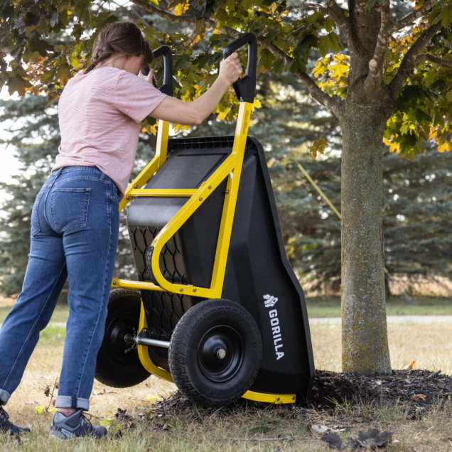 Person using a Gorilla black and yellow hand truck near a tree.