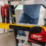 Yellow ladder with red Milwaukee 25 ft tape measure and screwdrivers attached.