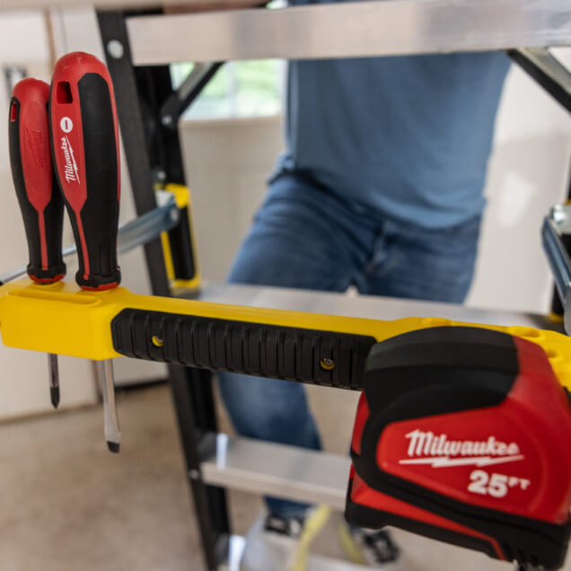 Yellow ladder with red Milwaukee 25 ft tape measure and screwdrivers attached.