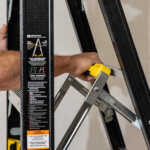 A hand gripping the yellow handle on a black Gorilla Made ladder, text visible on side.