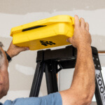 Adjusting a yellow Gorilla Made utility box atop a black ladder labeled "300 LB Load."