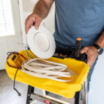 Yellow tool tray on a GF300 6B ladder with tools and electrical items, including a round white fixture.