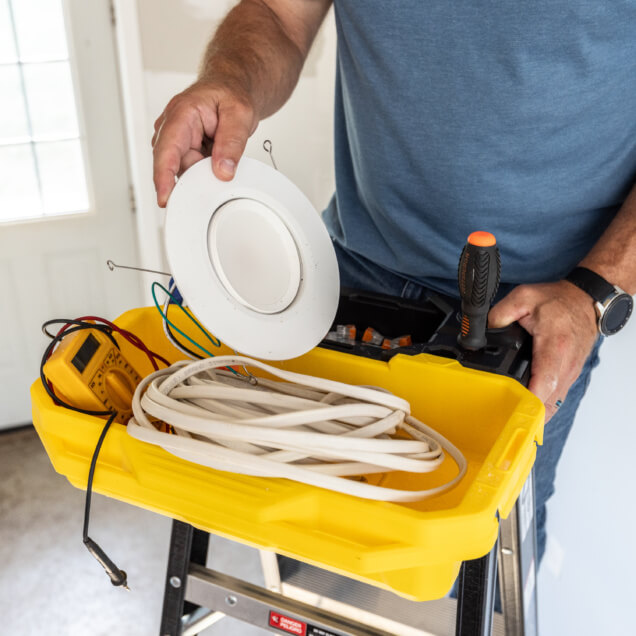 Yellow tool tray on a GF300 6B ladder with tools and electrical items, including a round white fixture.