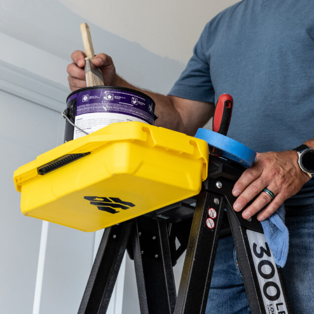 A yellow Gorilla Made tool box on a 300 lb capacity ladder with painting supplies.
