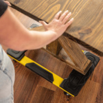 Yellow and black utility dolly supporting a wooden table on a wood floor.