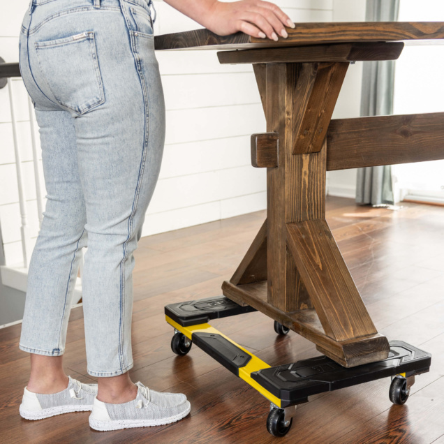Person moving a brown wooden table on a black and yellow wheeled dolly.