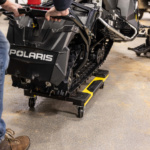 A snowmobile on a yellow and black cart with "POLARIS" text, in a garage setting.