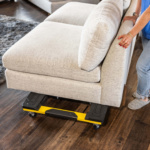A yellow and black Gorilla Made furniture dolly supports a beige sofa on wooden flooring.