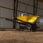 Yellow Gorilla wheelbarrow standing on dirt inside a metal-framed warehouse.