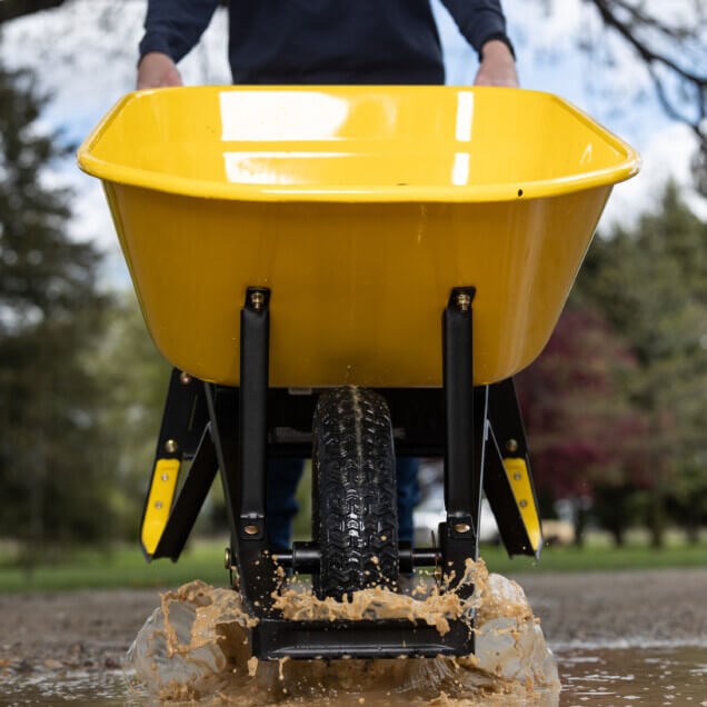 Yellow wheelbarrow splashing through a puddle, showcasing water resilience.