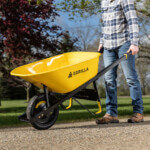 Yellow Gorilla wheelbarrow with "FLAT FREE" tire in use on gravel path.